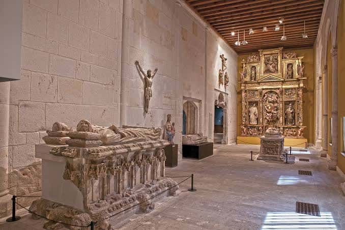Sala de exposiciones con sarcófago medieval y retablo dorado