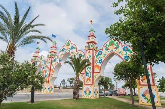 Arco de entrada principal del recinto ferial con decoración floral y palmeras