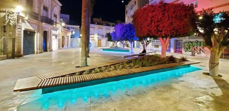 Área de descanso nocturna con banco integrado en fuente luminosa y árboles decorativos
