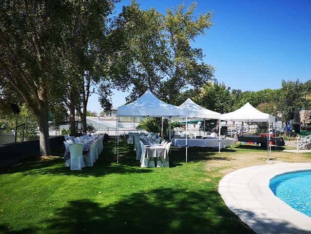 Terraza exterior con mesas dispuestas para evento bajo carpas blancas junto a una piscina