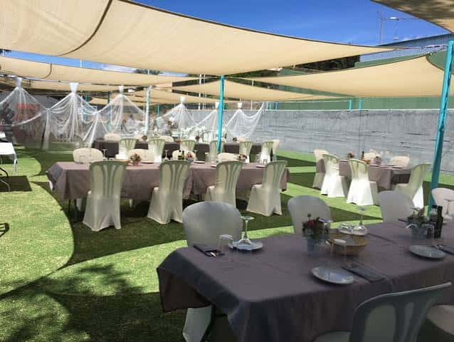 Salón al aire libre con mesas y sillas decoradas bajo toldos beige en Espacio Mentema