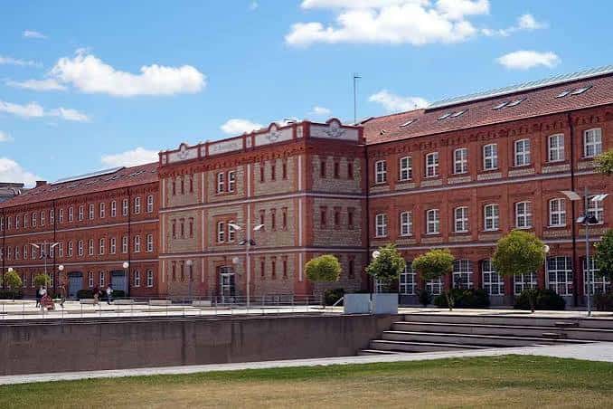 Vista lateral del edificio de ladrillo rojo con detalles arquitectónicos y jardines frontales