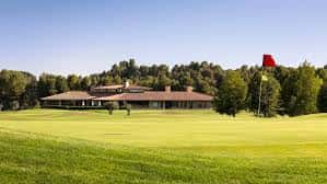 Vista del campo de golf con el club house y bandera roja en primer plano