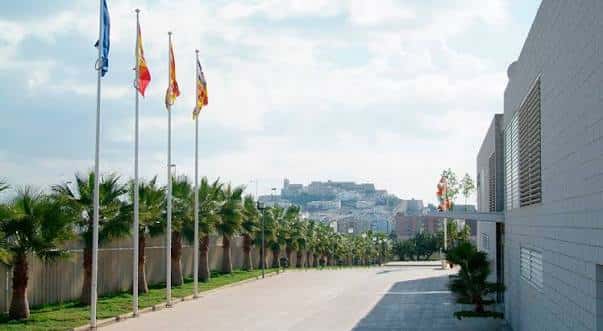 Avenida principal del recinto con banderas y palmeras bajo el sol