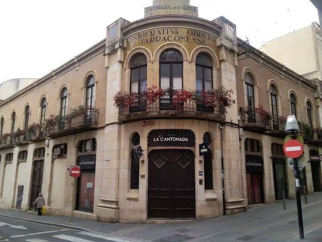 Vista exterior del edificio con balcones floridos y letrero histórico