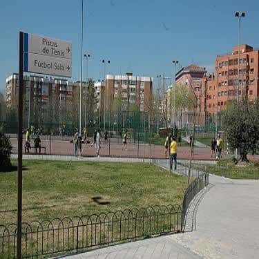 Vista exterior de las pistas deportivas al aire libre con césped y edificios residenciales al fondo