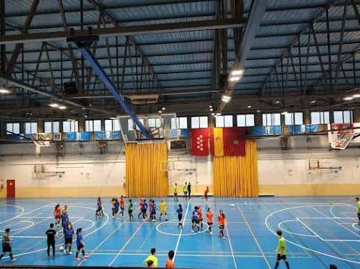 Interior del polideportivo mostrando una cancha de baloncesto con jugadores en actividad