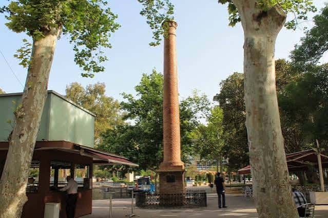 Chimenea histórica del Jardín de la Pólvora rodeada de árboles y kioscos