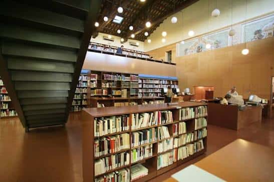 Interior de la biblioteca mostrando estanterías y zona de lectura en planta superior