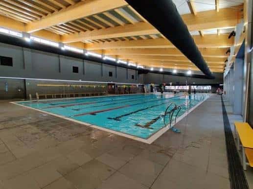 Piscina interior de competición con carriles marcados y estructura de madera en el techo