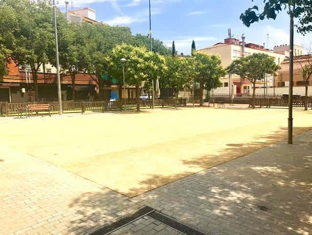 Vista general de la Plaça Onze de Setembre con árboles y bancos en un día soleado