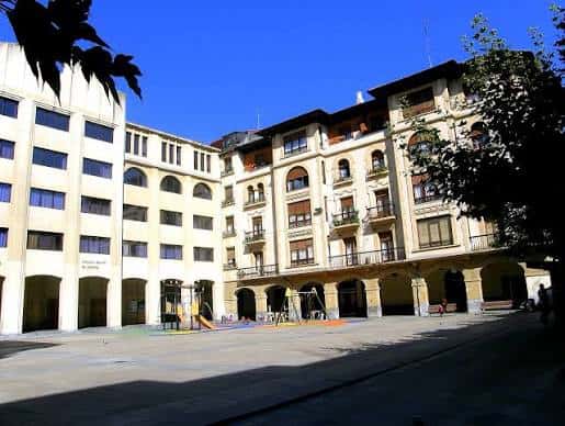 Vista actual de la Plaza de las Escuelas con el edificio principal y zona de juegos infantiles