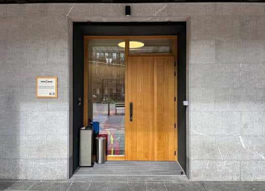 Entrada principal del edificio con puerta de madera y señalética institucional