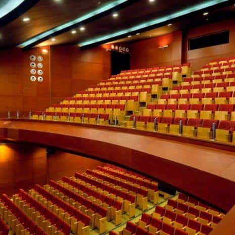 Interior del auditorio con butacas rojas y amarillas en gradas