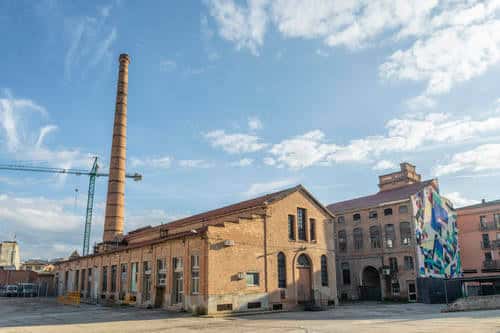 Vista exterior del complejo industrial con chimenea y mural colorido