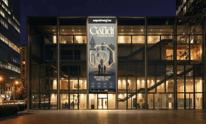 Fachada nocturna del Espai Imagina con iluminación cálida y cartel promocional del Codi Gaudí