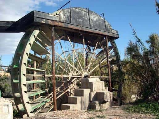 Detalle de una rueda de agua antigua con estructura metálica y vegetación circundante