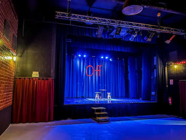 Escenario del auditorio OffCultura con iluminación azul y cortinas