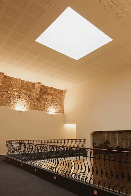 Detalle arquitectónico interior con balcón de hierro forjado y pared de piedra histórica iluminada
