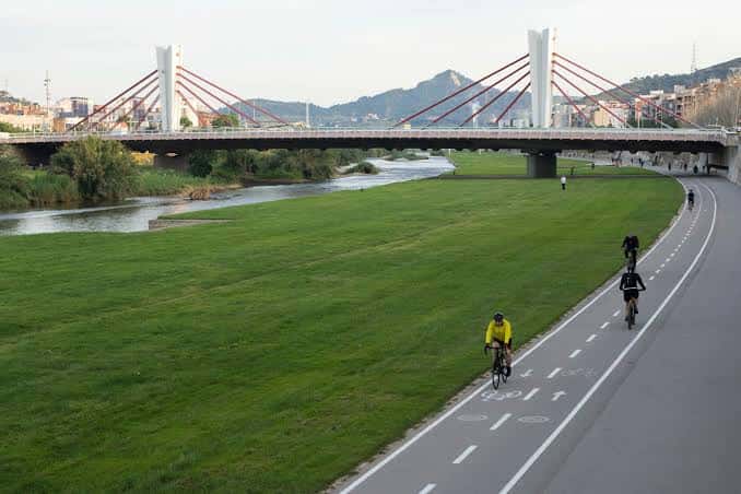 Ciclistas transitando por la senda junto al río con el puente de fondo