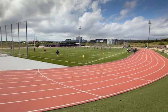 Vista panorámica de la pista de atletismo con césped central y cielo parcialmente nublado