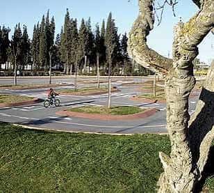 Vista del parque con ciclista pasando por una rotonda y cipreses al fondo