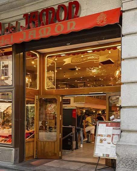 Fachada exterior del Museo del Jamón en Madrid con letrero rojo y entrada iluminada