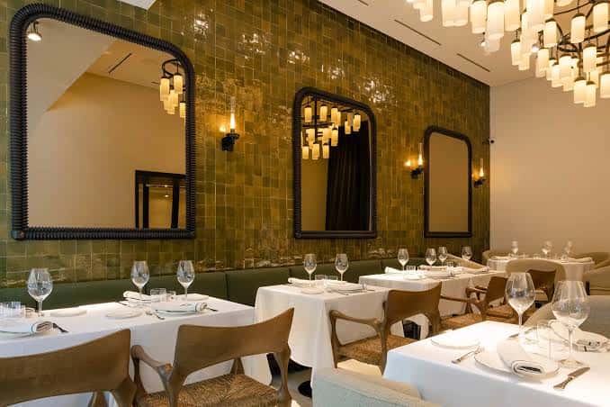 Sala de comedor elegante con paredes revestidas en azulejos verdes y espejos decorativos