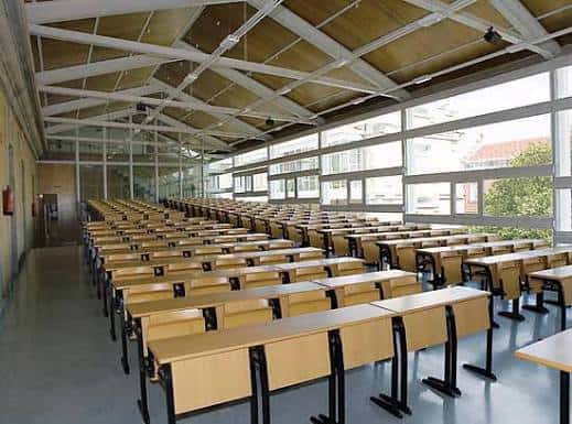 Aula magna o salón de actos con filas de pupitres y techo estructural visible