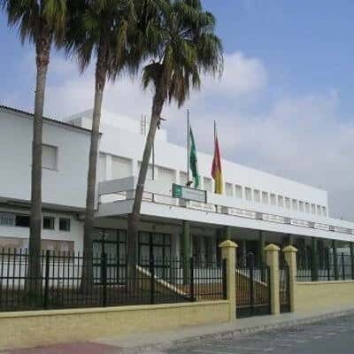 Vista exterior del edificio principal del IES Juan de la Cierva con palmeras y banderas