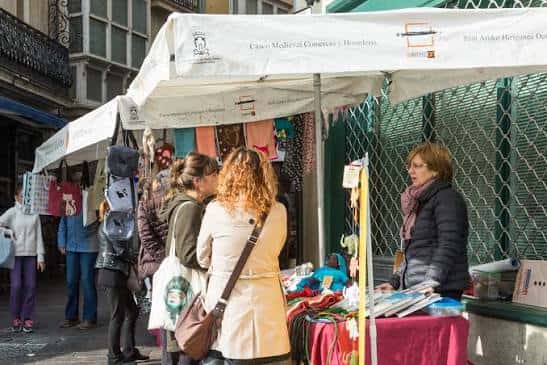 Puestos comerciales bajo toldos en el exterior del mercado con clientes comprando