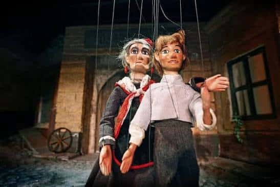 Dos títeres de cuerda en escena representando una obra teatral