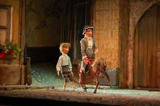 Títeres en escena: un niño caminando junto a un hombre montado en burro
