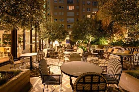 Terraza exterior iluminada por la noche con mesas y árboles