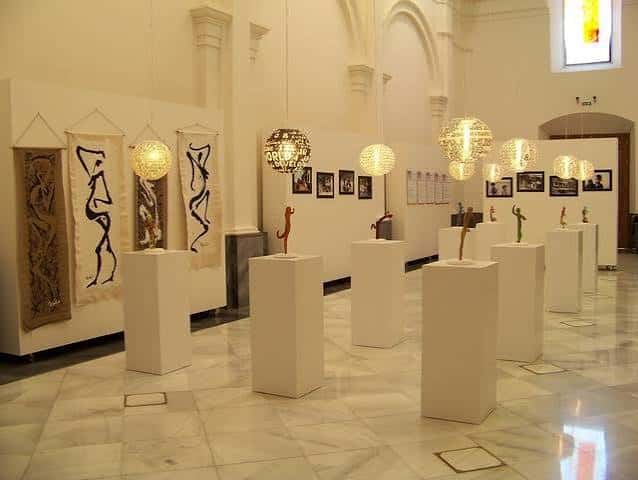 Interior de la capilla con exposición de arte y esculturas en pedestales blancos