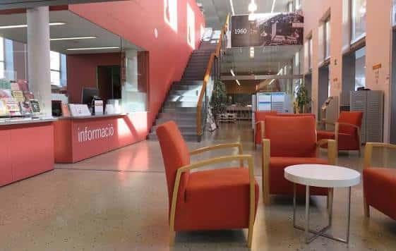 Interior del hall principal con mostrador de información, escalera y zona de descanso con sillones naranjas
