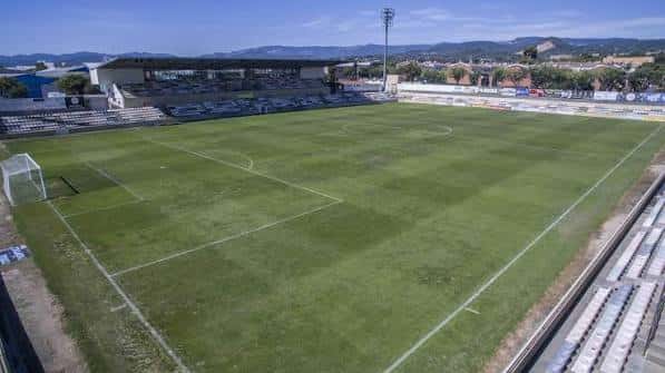Campo de fútbol con gradas laterales y fondo montañoso en el Estadi Municipal de Reus