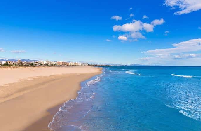 Vista panorámica de la Playa de Almardá con arena dorada y aguas turquesas bajo un cielo azul despejado