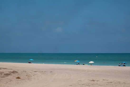 Playa amplia con sombrillas dispersas y olas suaves rompiendo en la orilla