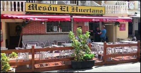 Fachada exterior del Mesón El Huertano con terraza y toldos rojos