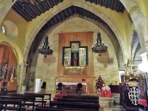 Interior de la iglesia mostrando el altar mayor, bóvedas de piedra y lámparas colgantes