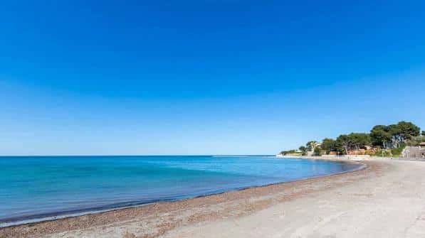 Vista panorámica de la Playa de la Marineta Cassiana con arena dorada y mar turquesa bajo un cielo despejado