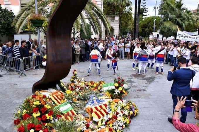 Ceremonia en la plaza con ofrenda floral y grupo de personas vestidas tradicionalmente