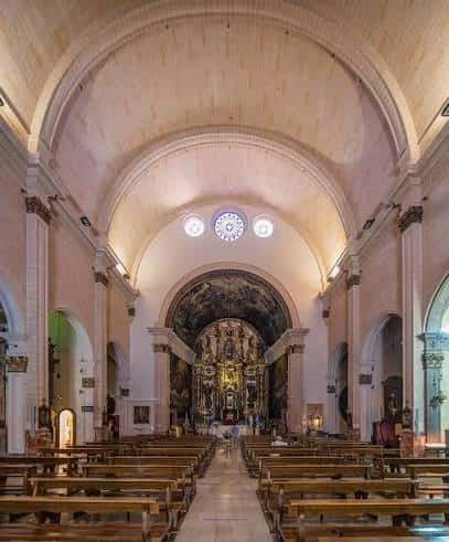 Perspectiva longitudinal del interior de la basílica con bancos y cúpula iluminada