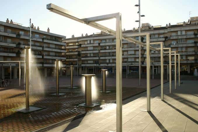 Detalle de fuentes y estructuras metálicas en la plaza durante el día
