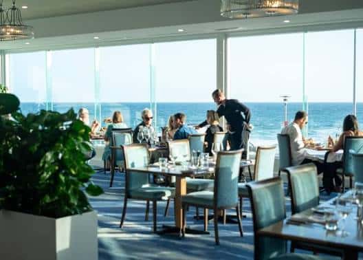 Interior del restaurante con vistas al mar y comensales disfrutando de una comida