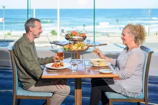Pareja degustando afternoon tea frente a la playa en NOAH'S on the Beach