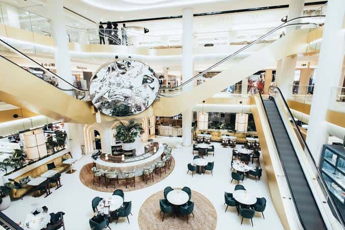 Interior del centro comercial con escaleras mecánicas, zona de cafetería y decoración elegante