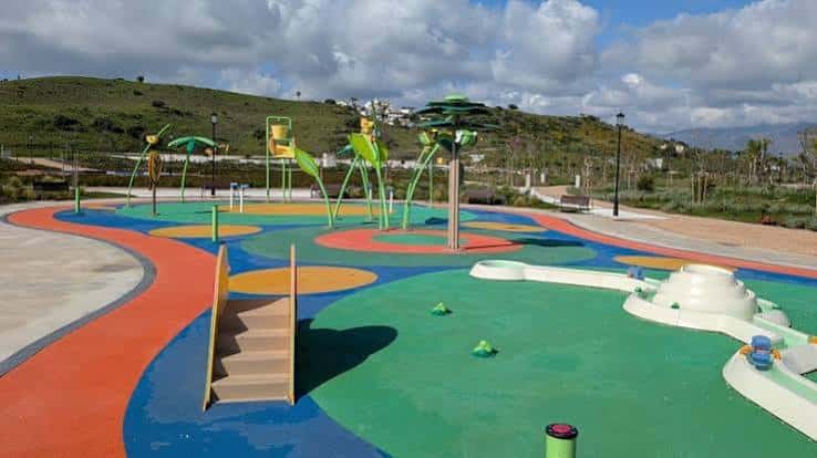 Vista amplia de la zona de juegos infantil con suelo de caucho multicolor y estructuras verdes