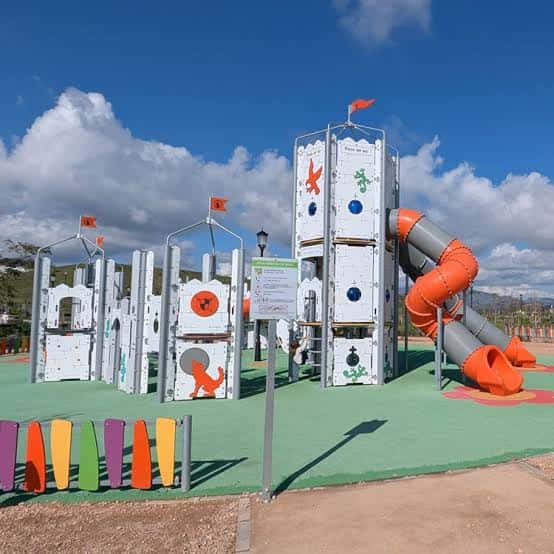 Estructura de juego infantil tipo castillo con toboganes naranjas bajo un cielo azul despejado